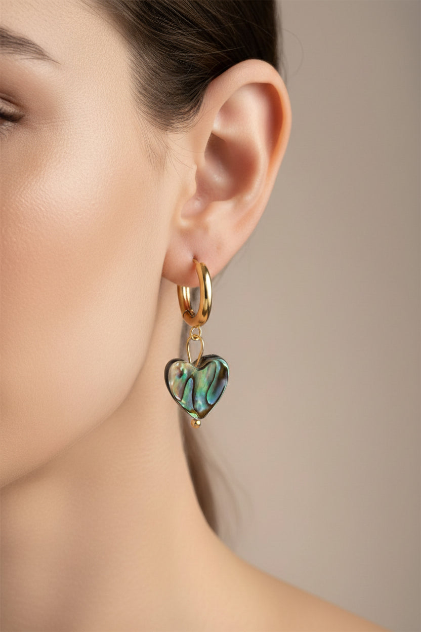 Close-up of abalone shell heart drop earrings showcasing natural iridescent shell tones in green, blue, and violet with polished 18K PVD gold plating.