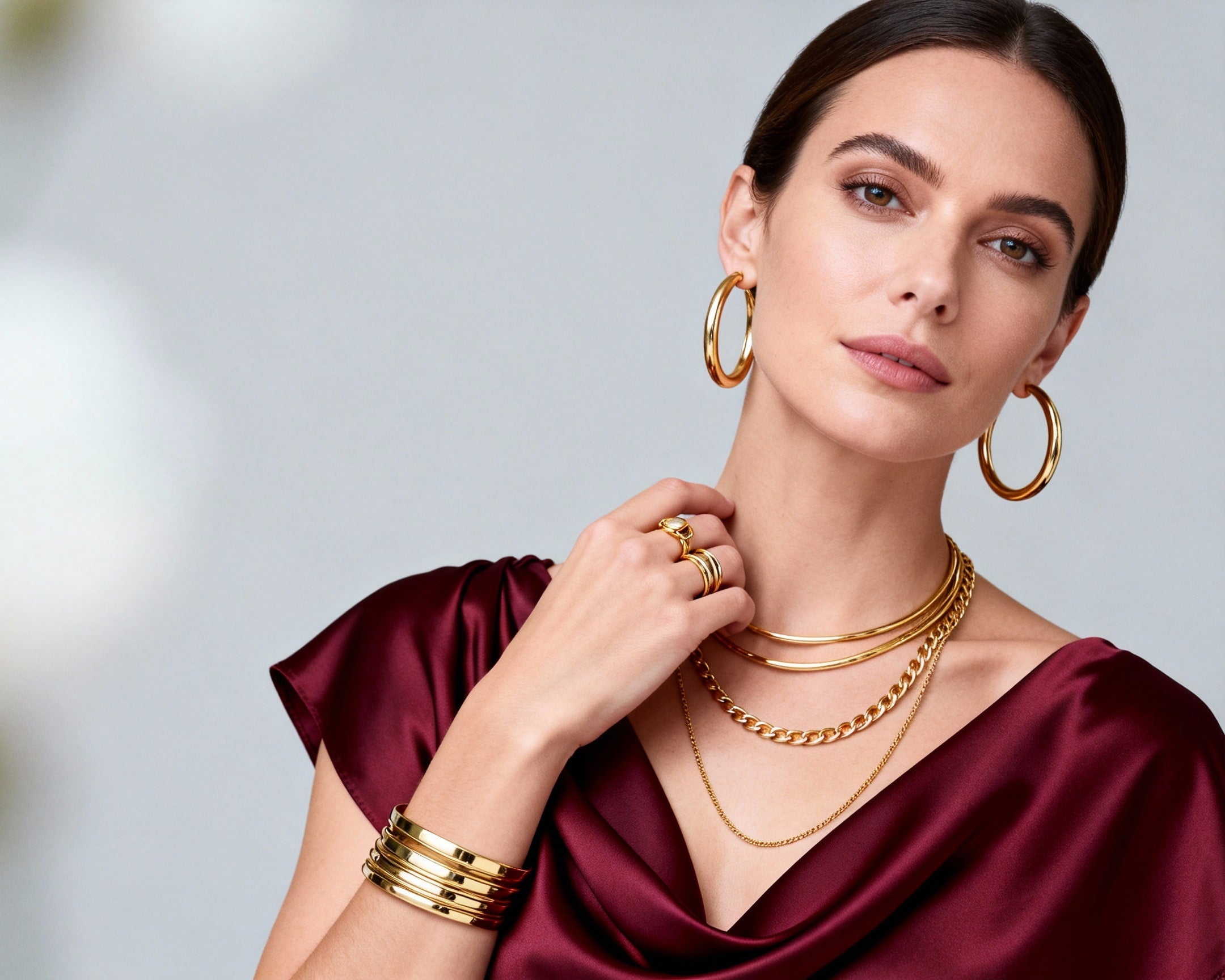 Glistia woman wearing gold jewelry including earrings, necklace, and bracelet against a neutral background