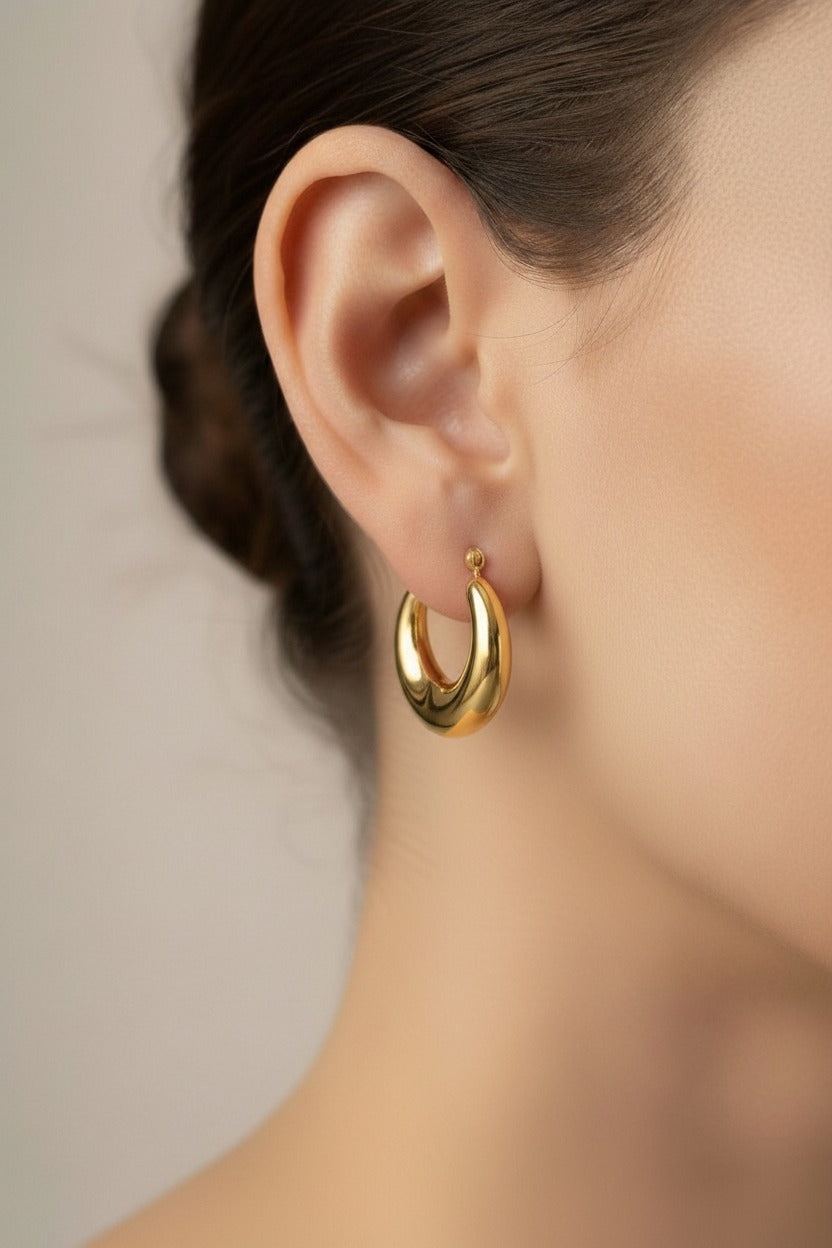 Bold crescent hoop earrings in 18K PVD gold plated stainless steel worn on ear, sculptural curved hoop design