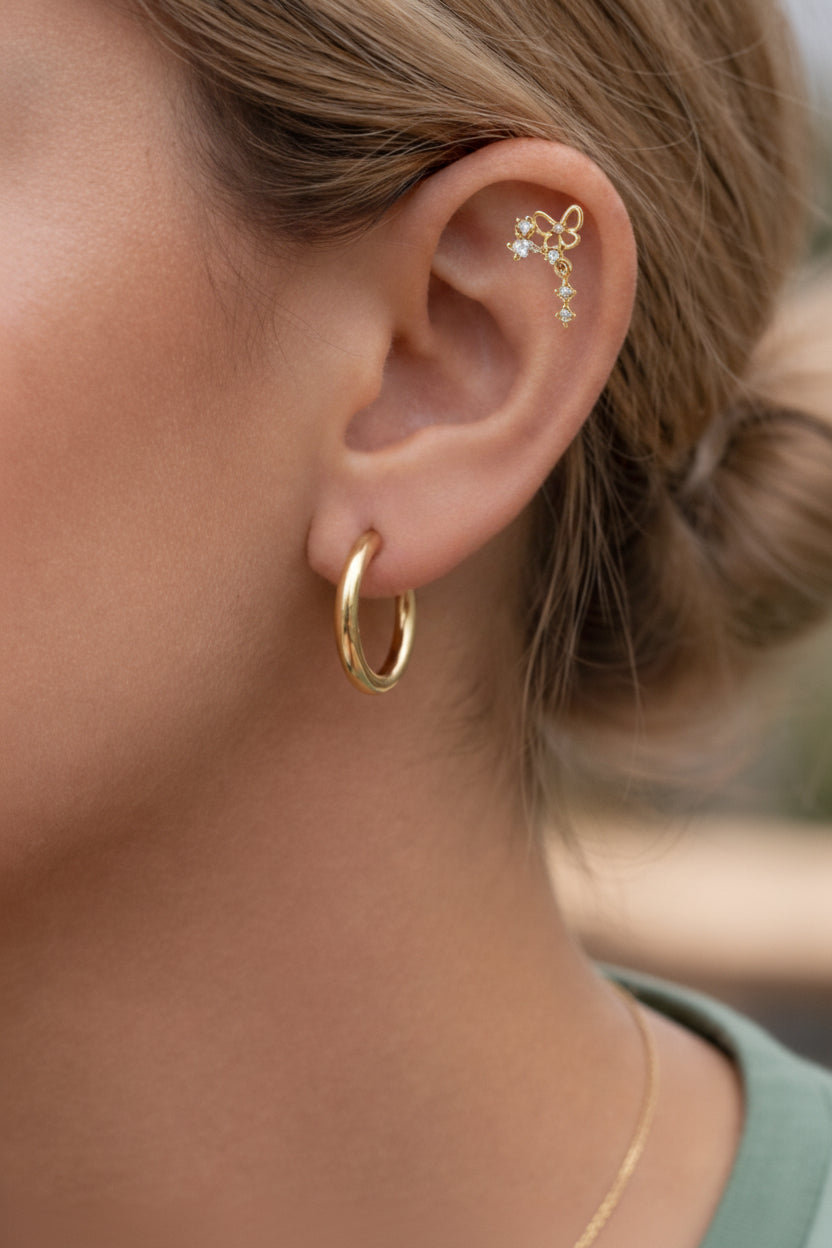 Butterfly drop piercing earrings worn on ear, showcasing delicate butterfly motif and crystal drop design in 18K PVD gold plated stainless steel.