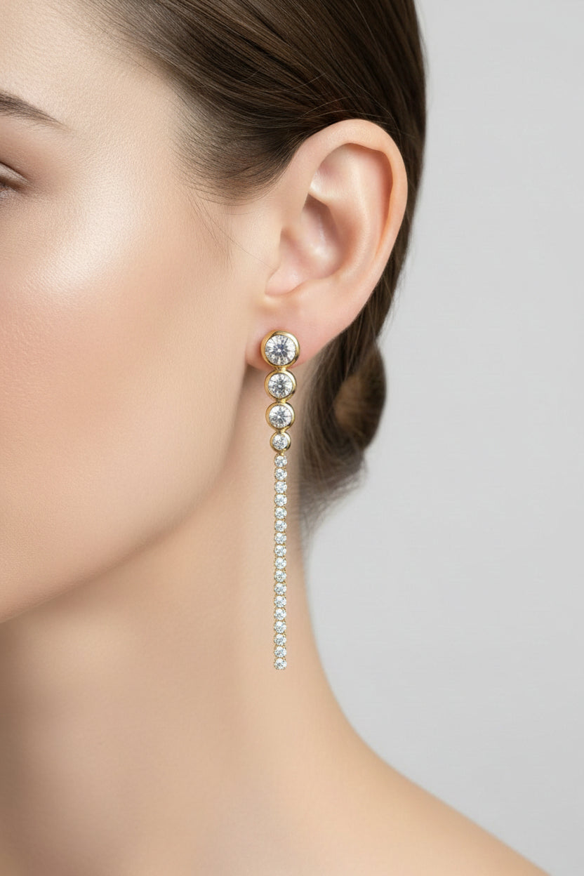Close-up of long crystal drop earrings showcasing polished 18K PVD gold plating and sparkling clear crystals in a fluid drop design.