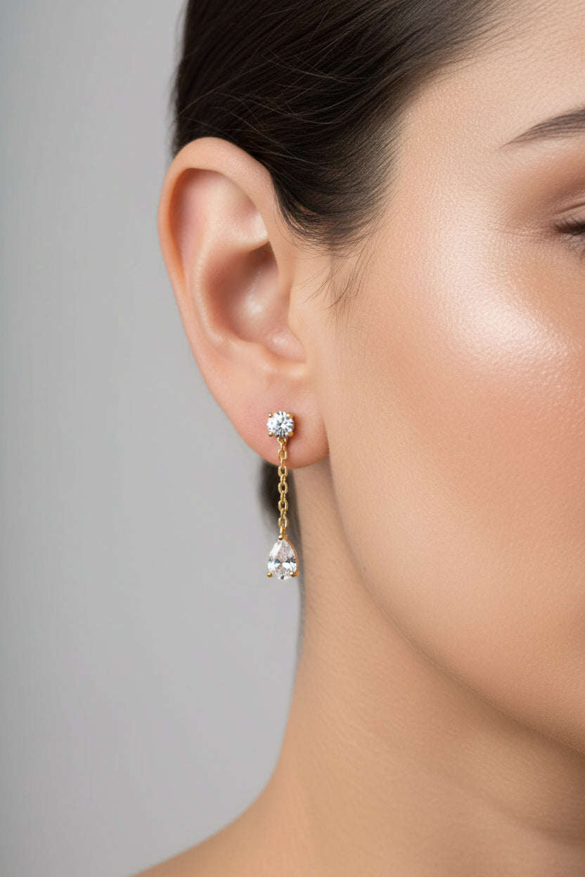 Dangle crystal chain stud earrings worn on ear, showcasing delicate chain drop design with cubic zirconia stones in 18K PVD gold plated stainless steel