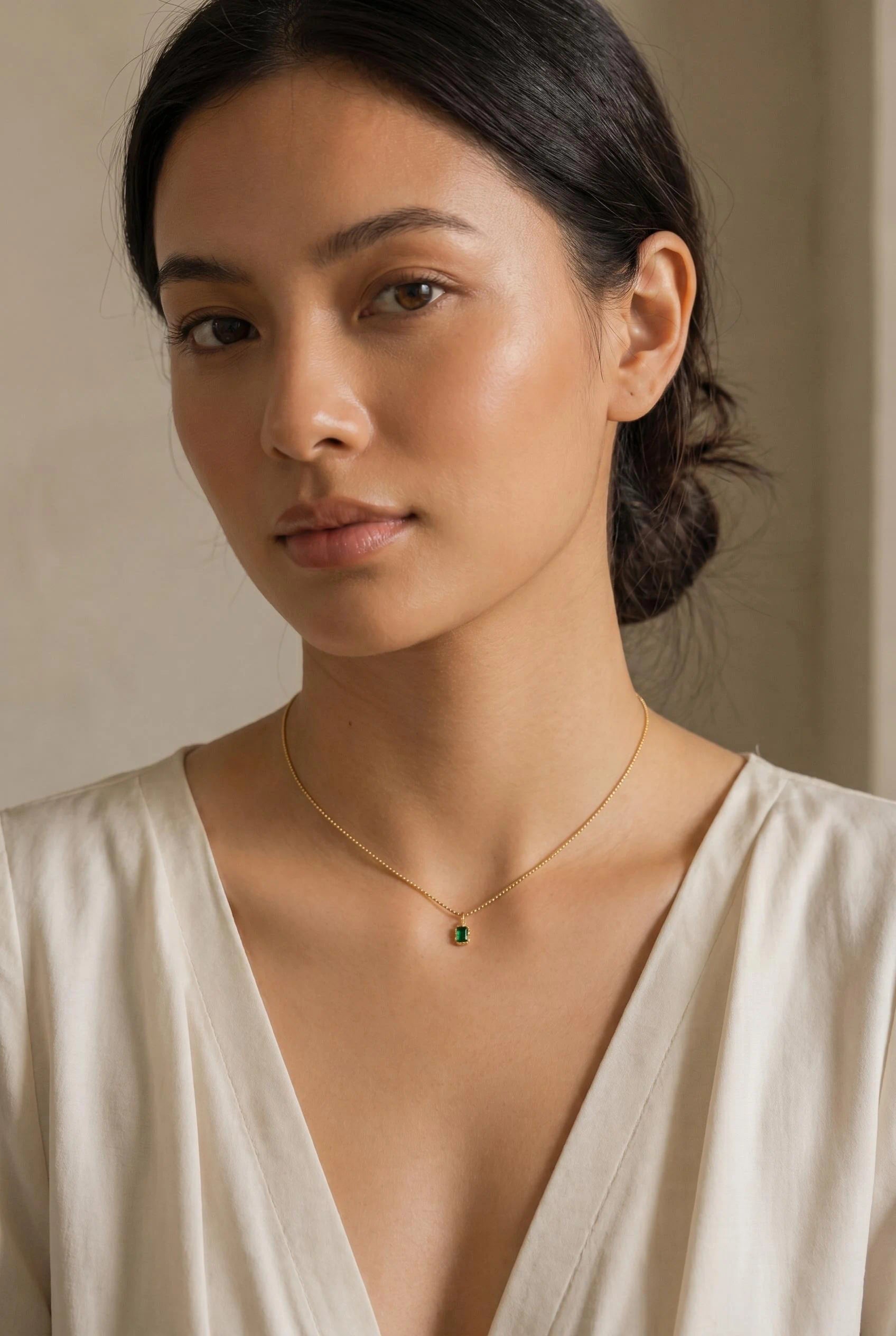 Emerald Radiance Pendant Necklace in 18K PVD gold plated finish featuring a green emerald-cut stone pendant worn on a female model neckline with luxury minimal styling.