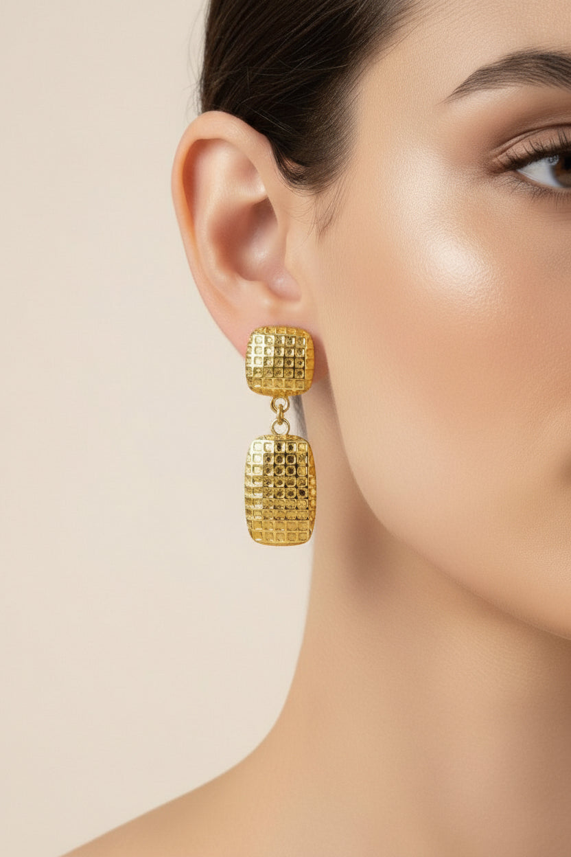 Close-up of geometric drop earrings showcasing polished 18K PVD gold plating and a textured rectangular grid design.