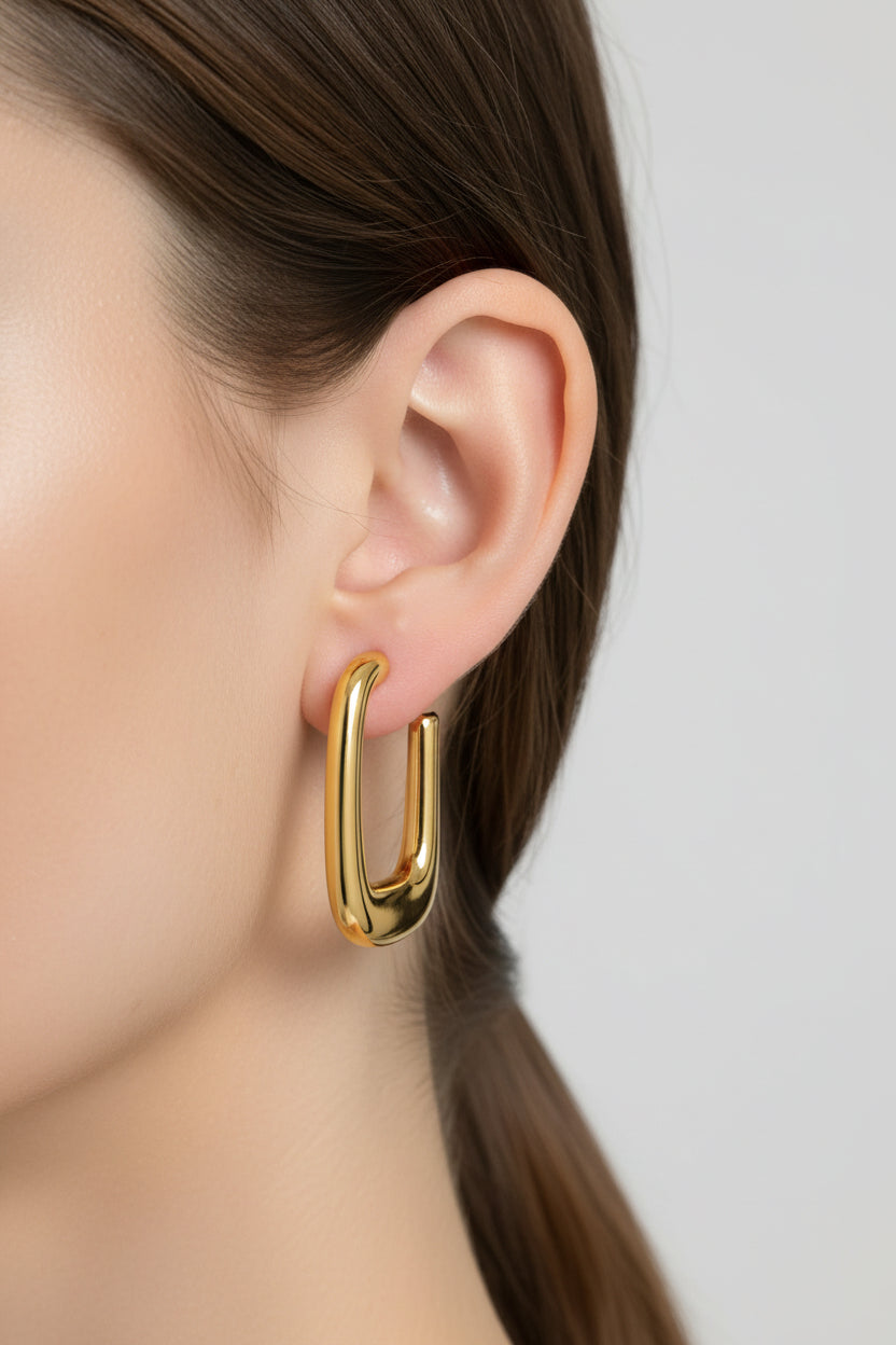 Geometric rectangular hoop earrings worn on ear, crafted from stainless steel with 18K PVD gold plating and a softly rounded rectangular silhouette.