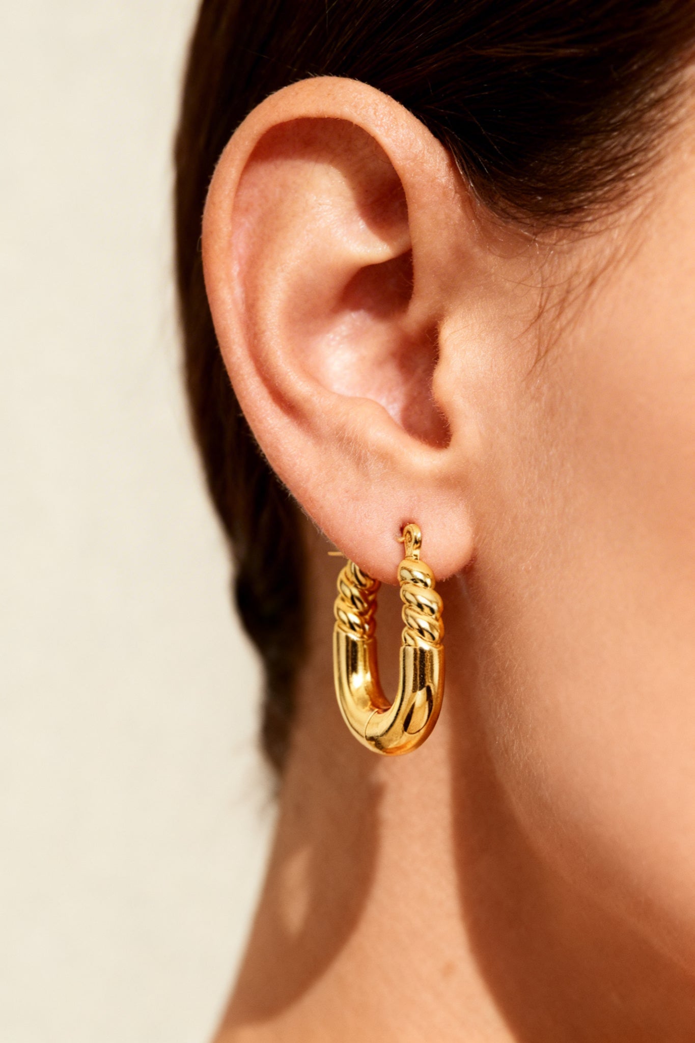 GLISTIA U-shaped twisted hoop earrings in 18K PVD gold plated stainless steel worn on ear
