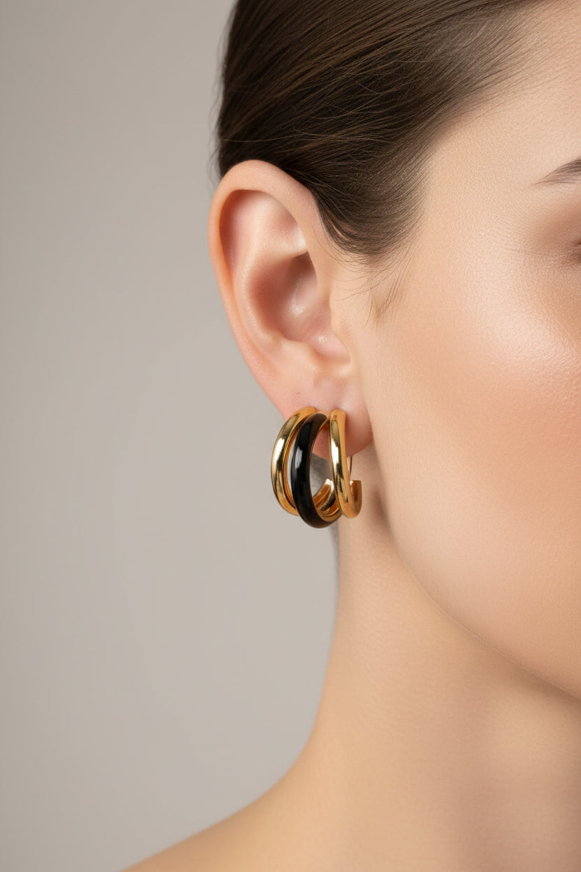 Close-up of double C-hoop earrings in stainless steel with 18K PVD gold plating and black enamel, showcasing a modern layered contrast design
