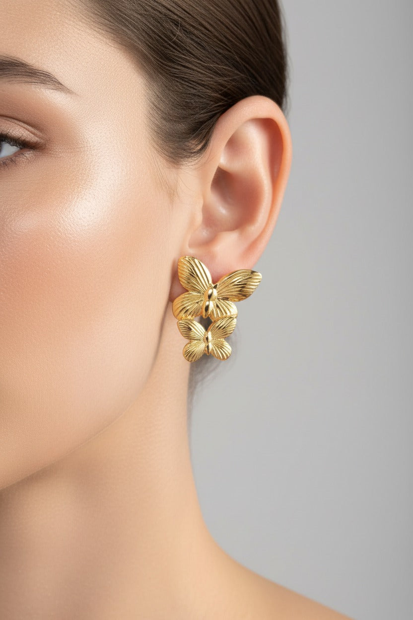 Gold butterfly stud earrings worn on ear, showcasing double butterfly motif with 18K PVD gold plated finish