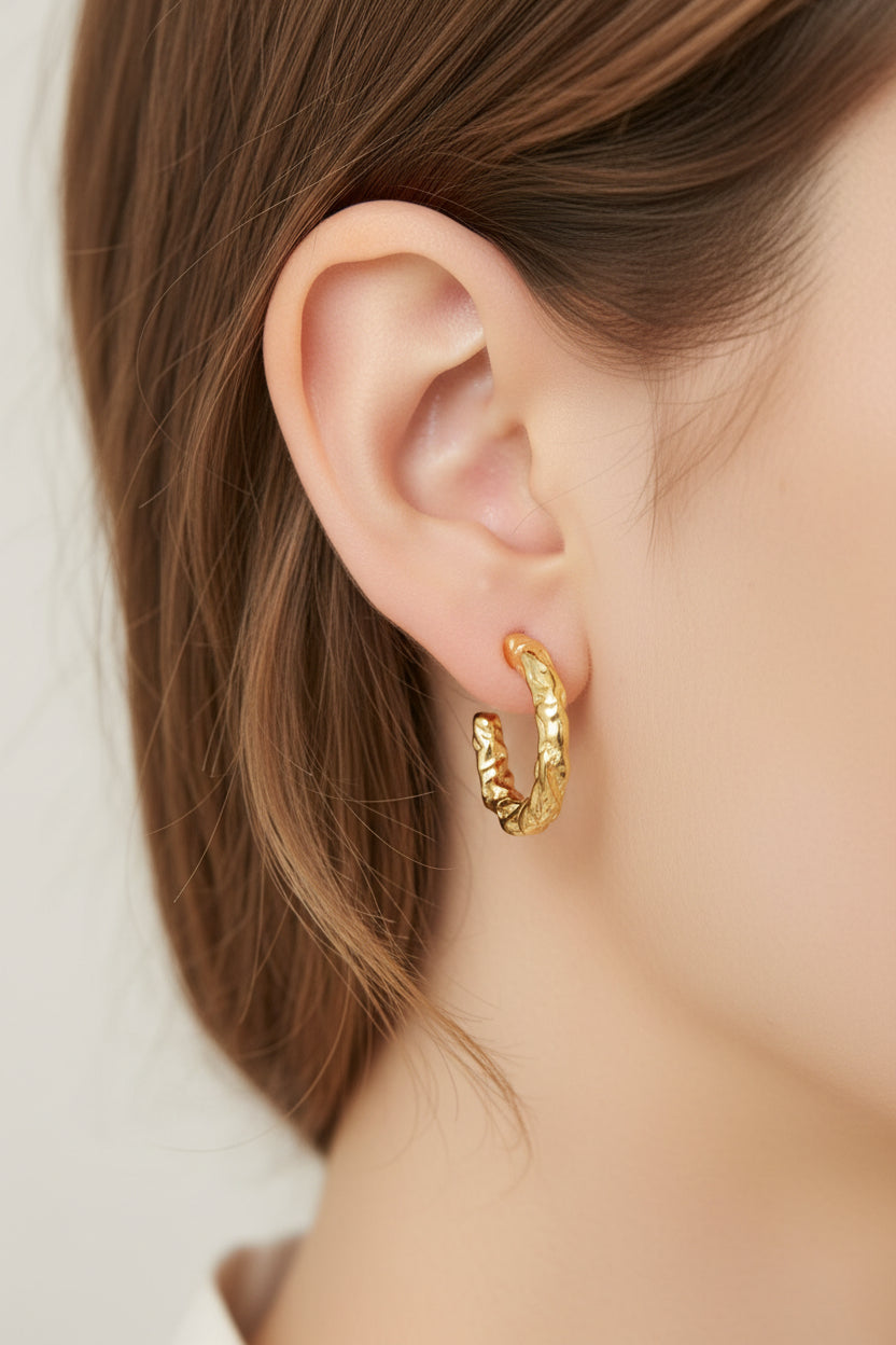 Close-up of molten textured hoop earrings in 18K PVD gold plated stainless steel, showcasing an organic sculptural design with light-catching texture