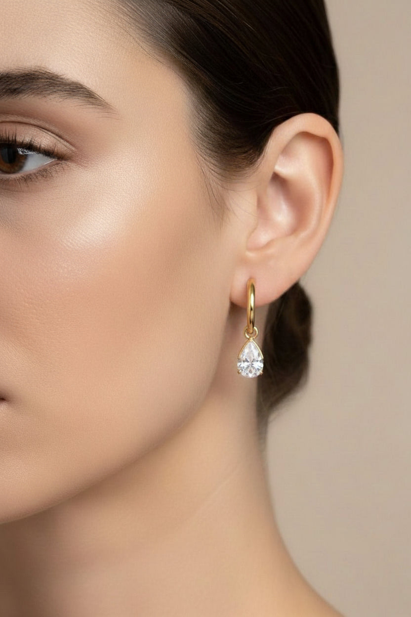 Close-up of hoop earrings with teardrop crystal drop in 18K PVD gold plated stainless steel, showcasing a clear crystal charm and elegant minimalist design