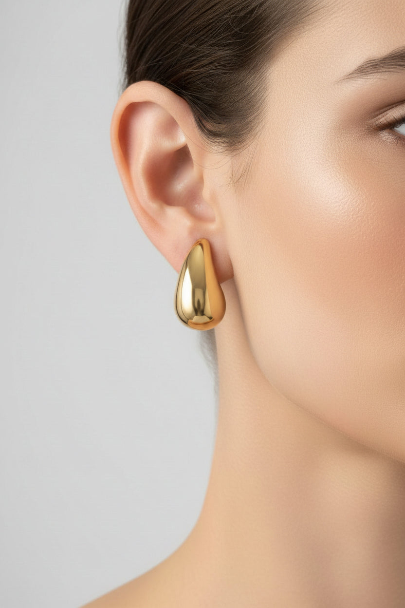 Gold teardrop stud earrings worn on ear, showcasing minimalist sculptural design with 18K PVD gold plated finish