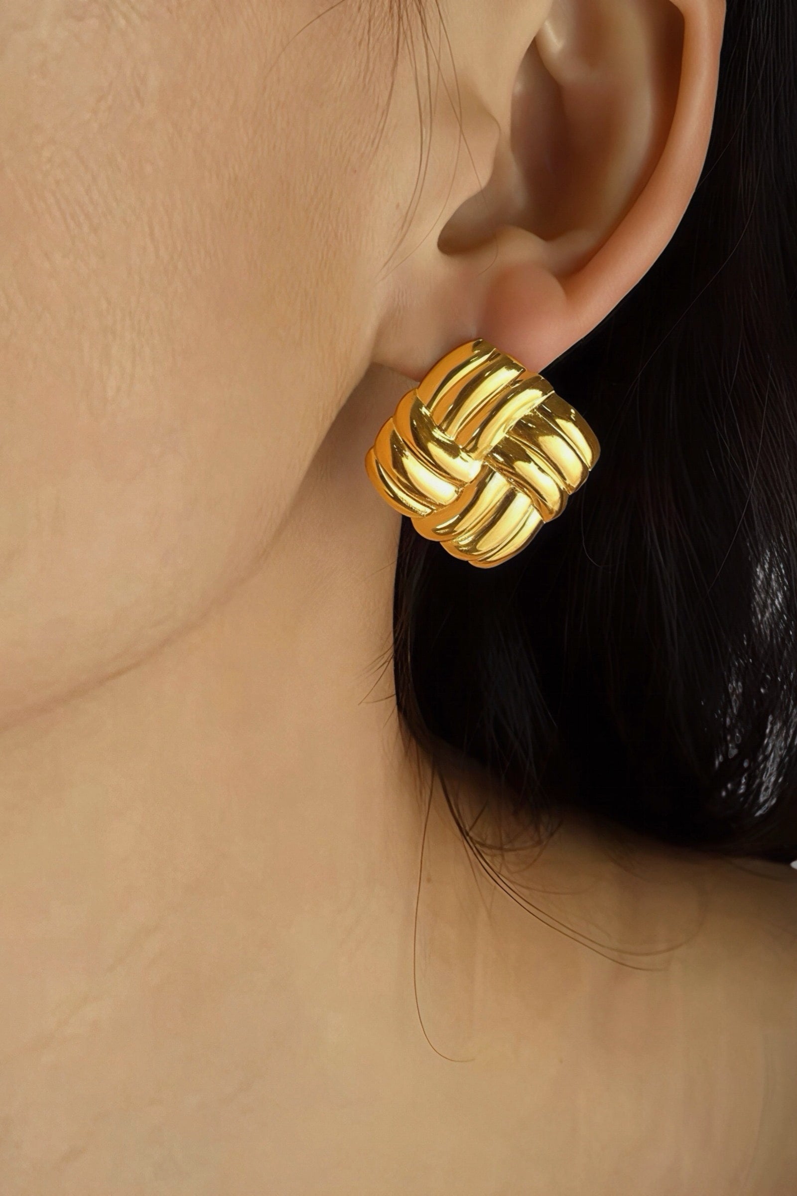 Close-up of model wearing gold woven square stud earrings crafted from stainless steel with a polished PVD 18K gold plated finish, showcasing interlaced design and radiant shine – GLISTIA.