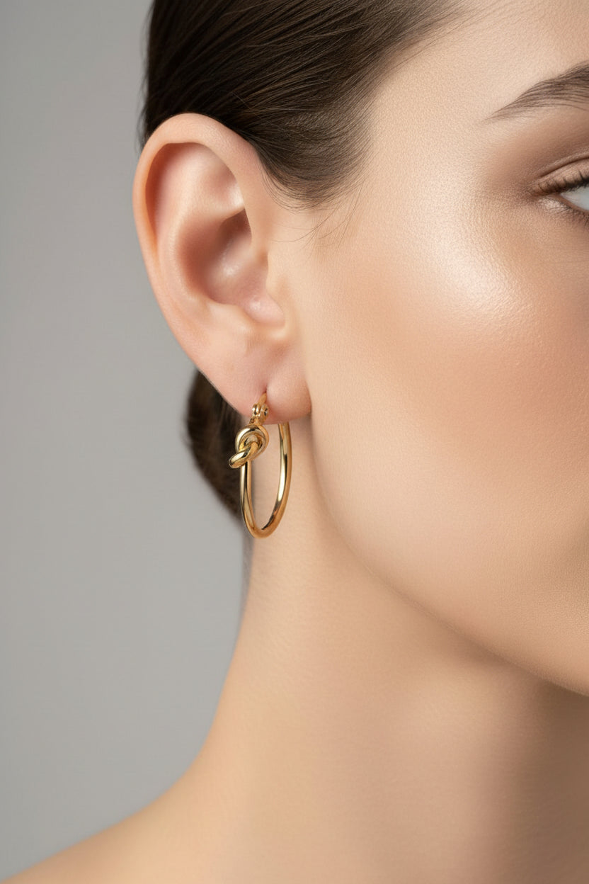 Close-up of hoop earrings with knot detail in 18K PVD gold plated stainless steel, showcasing a minimalist polished finish and modern silhouette