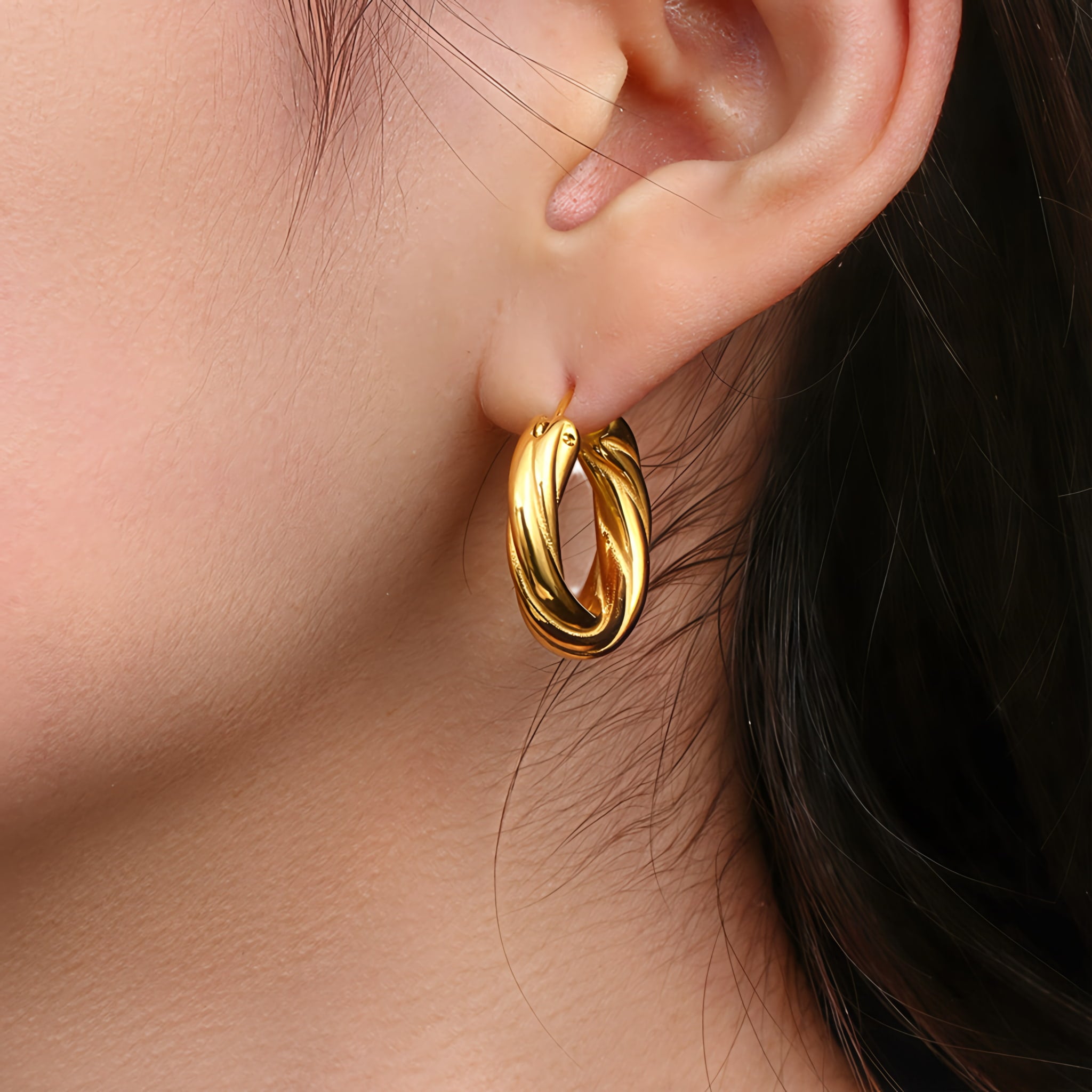 Model wearing large twisted gold hoop earrings, featuring a bold rope-style design with a polished 18K PVD gold-plated stainless-steel finish GLISTIA