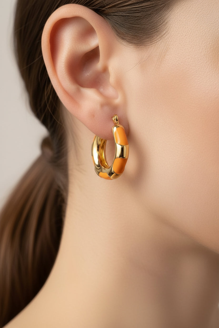 Close-up of bamboo-style hoop earrings in 18K PVD gold plated stainless steel, showcasing glossy orange enamel accents and textured gold finish
