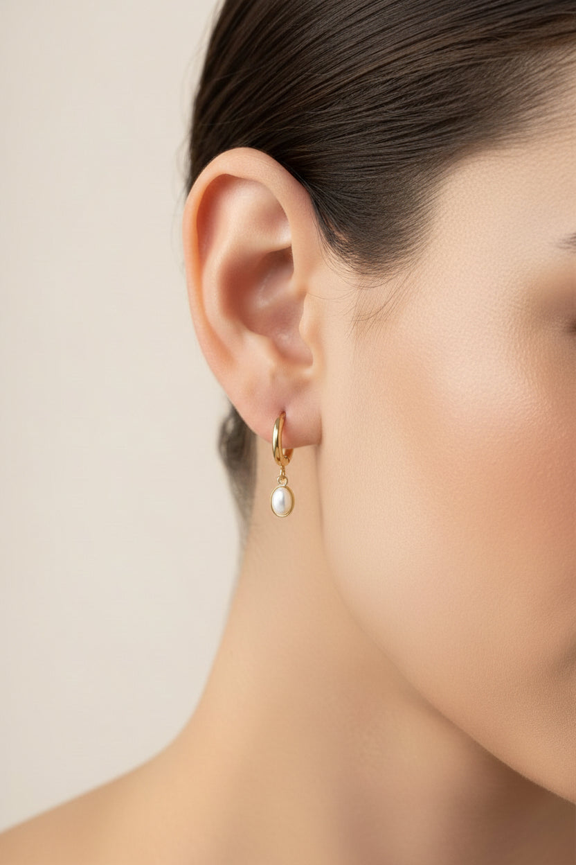 Close-up of gold oval drop hoop earrings showcasing polished 18K PVD gold plating and a minimalist oval drop design.