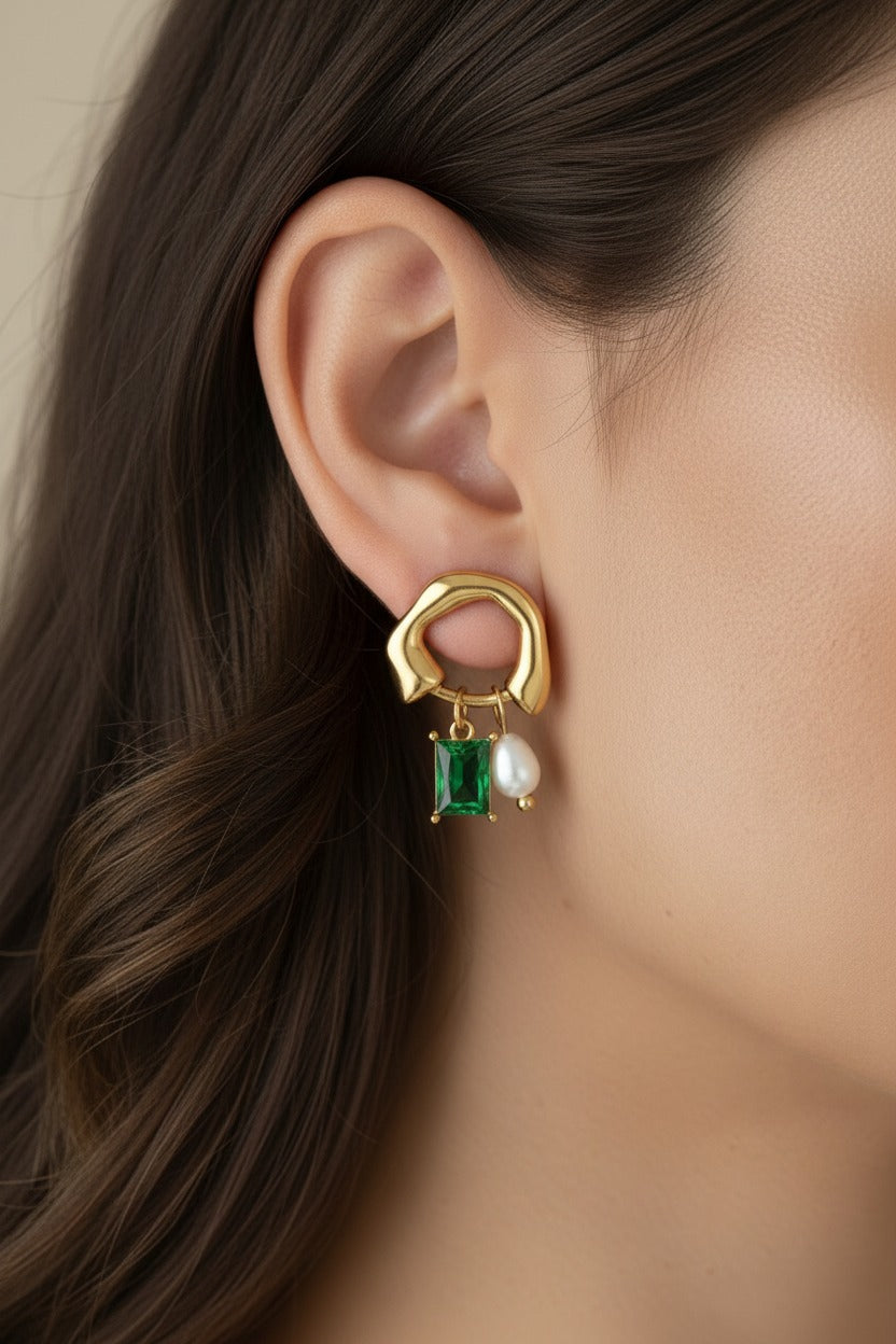 Close-up view of geometric hoop drop earrings crafted from stainless steel with 18K PVD gold plating, featuring a freshwater pearl and emerald green cubic zirconia.