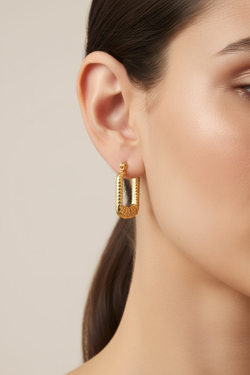 Close-up of rectangular hoop earrings in 18K PVD gold plated stainless steel, showcasing a modern geometric shape with textured surface detail