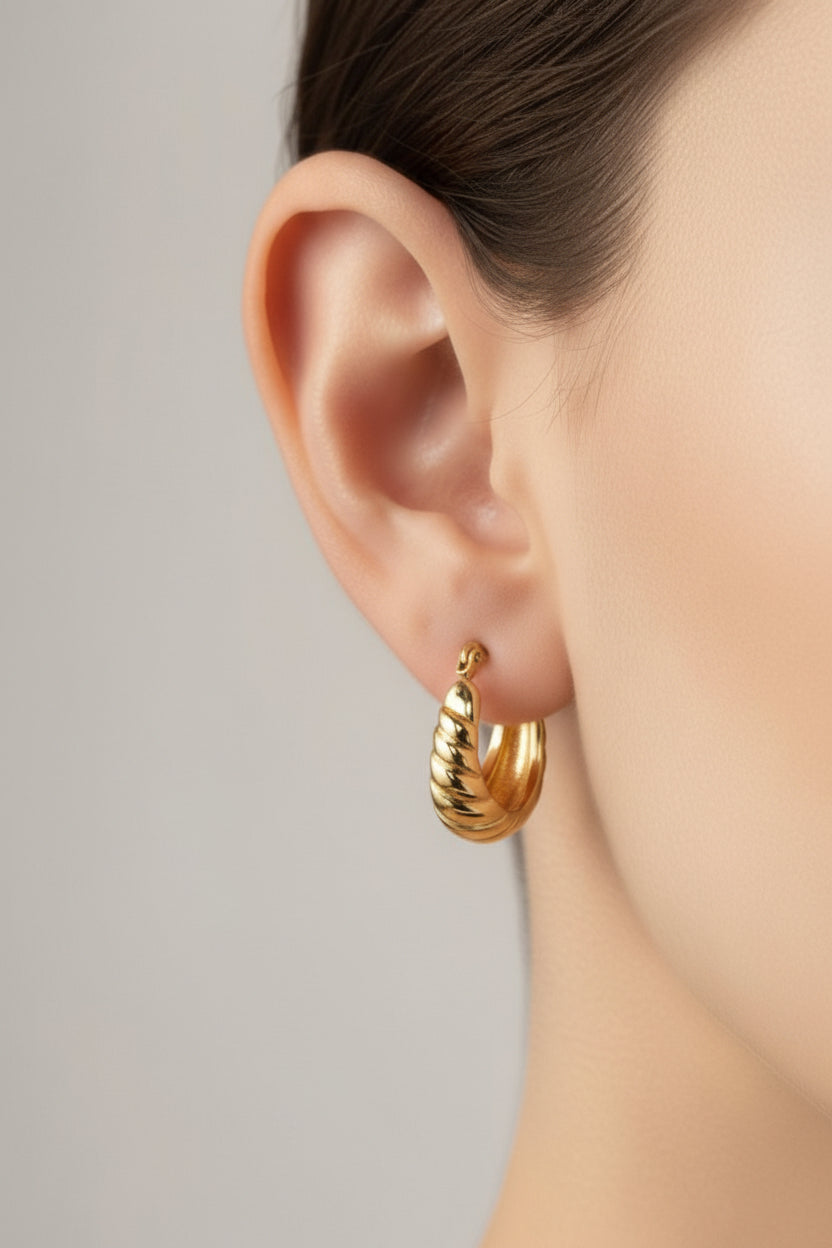 Close-up of ribbed hoop earrings in 18K PVD gold plated stainless steel, showcasing a puffed textured surface and polished gold tone