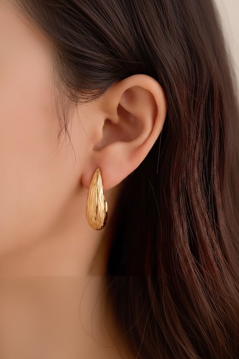 Sculpted teardrop earrings worn on ear, crafted from stainless steel with 18K PVD gold plating and textured curved design