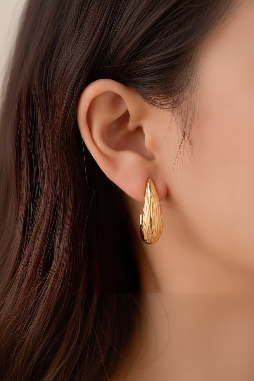 Side view of sculpted teardrop earrings in 18K PVD gold plated stainless steel with fluid silhouette and textured finish