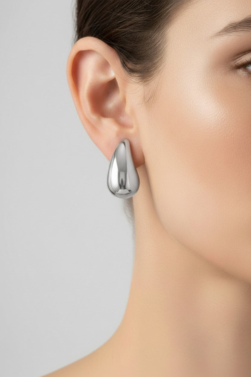 Silver teardrop stud earrings worn on ear, showcasing minimalist sculptural design with polished stainless steel finish