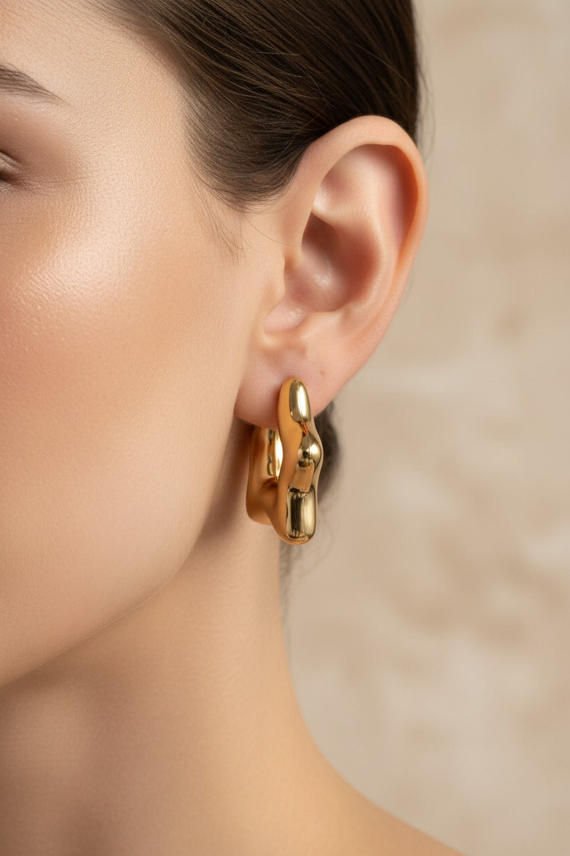 Stellar gold hoop earrings worn on ear, crafted from stainless steel with 18K PVD gold plating and sculptural star inspired curves.