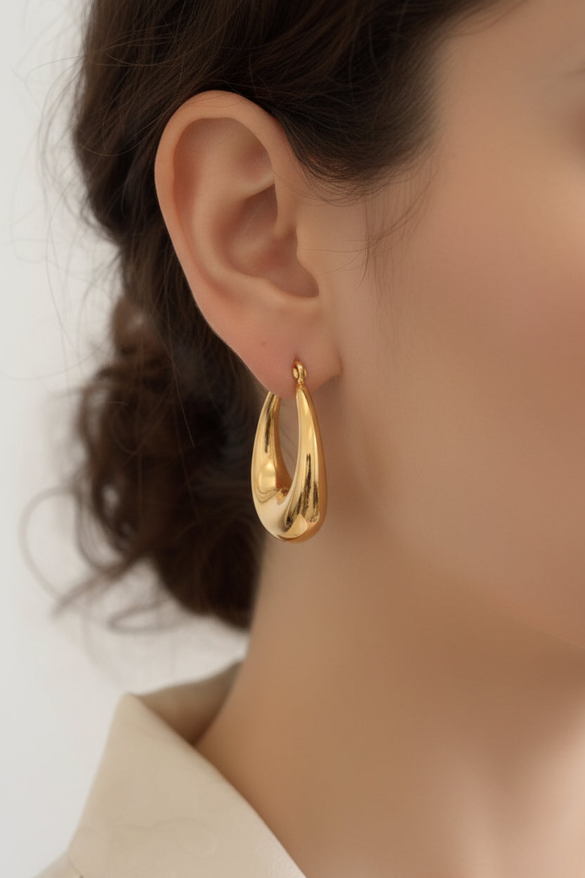 Teardrop statement hoop earrings in 18K PVD gold plated stainless steel worn on ear, featuring a sculpted high-polish dome design.