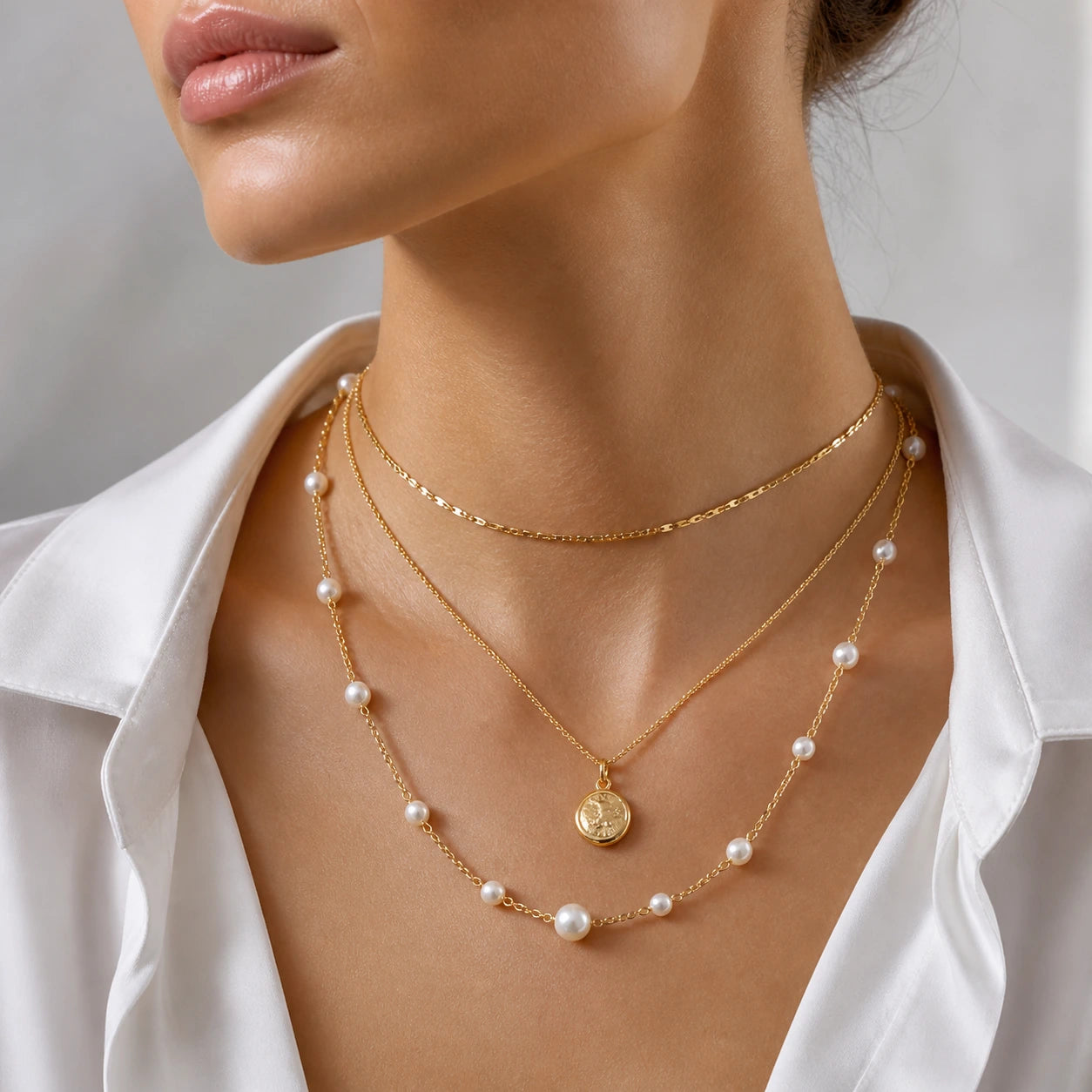 Close-up of a woman wearing a gold necklace with pearl accents and a white shirt.