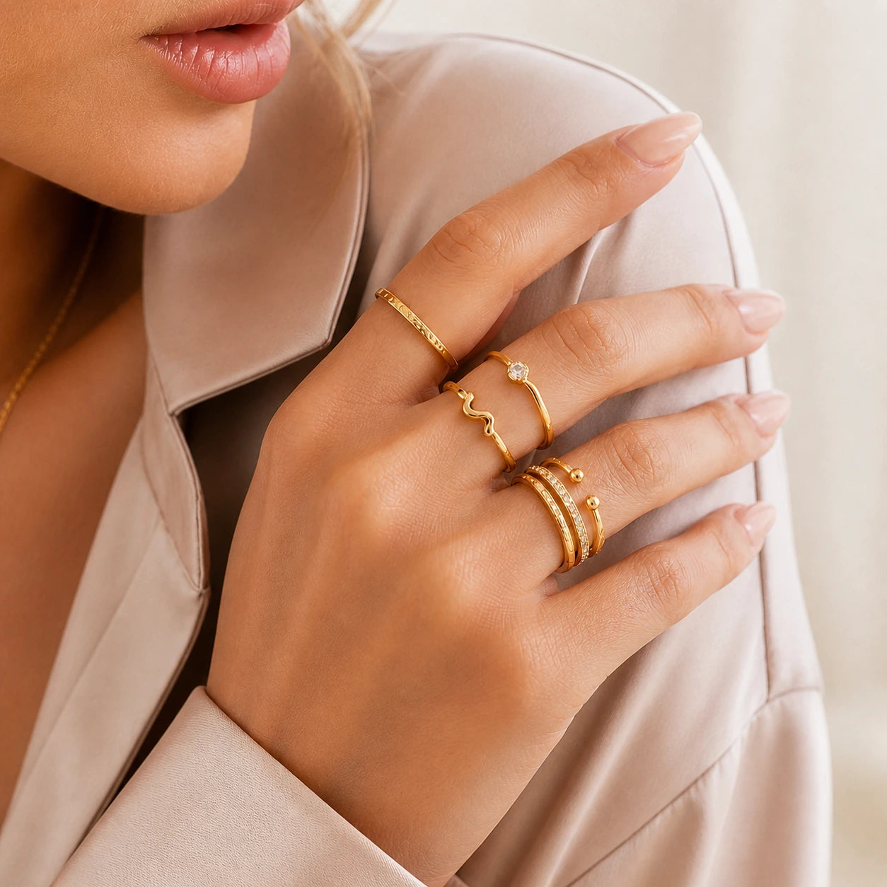 Close-up of a hand wearing gold rings on a neutral background