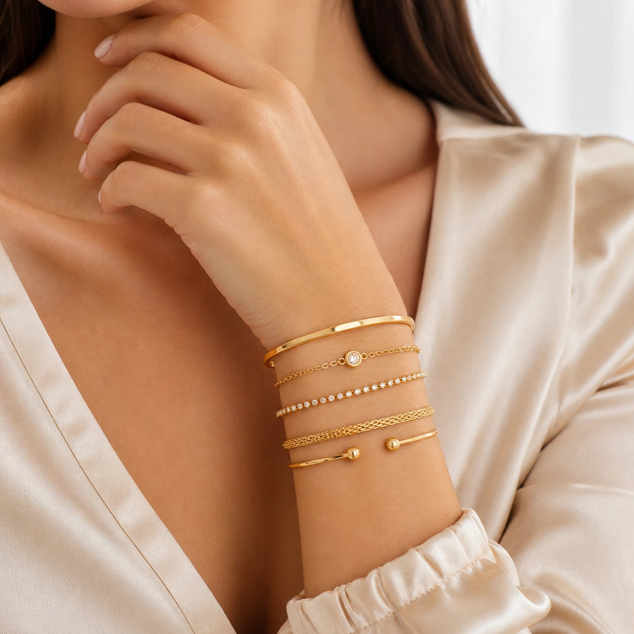 Close-up of a woman's arm wearing multiple gold bracelets on a neutral background