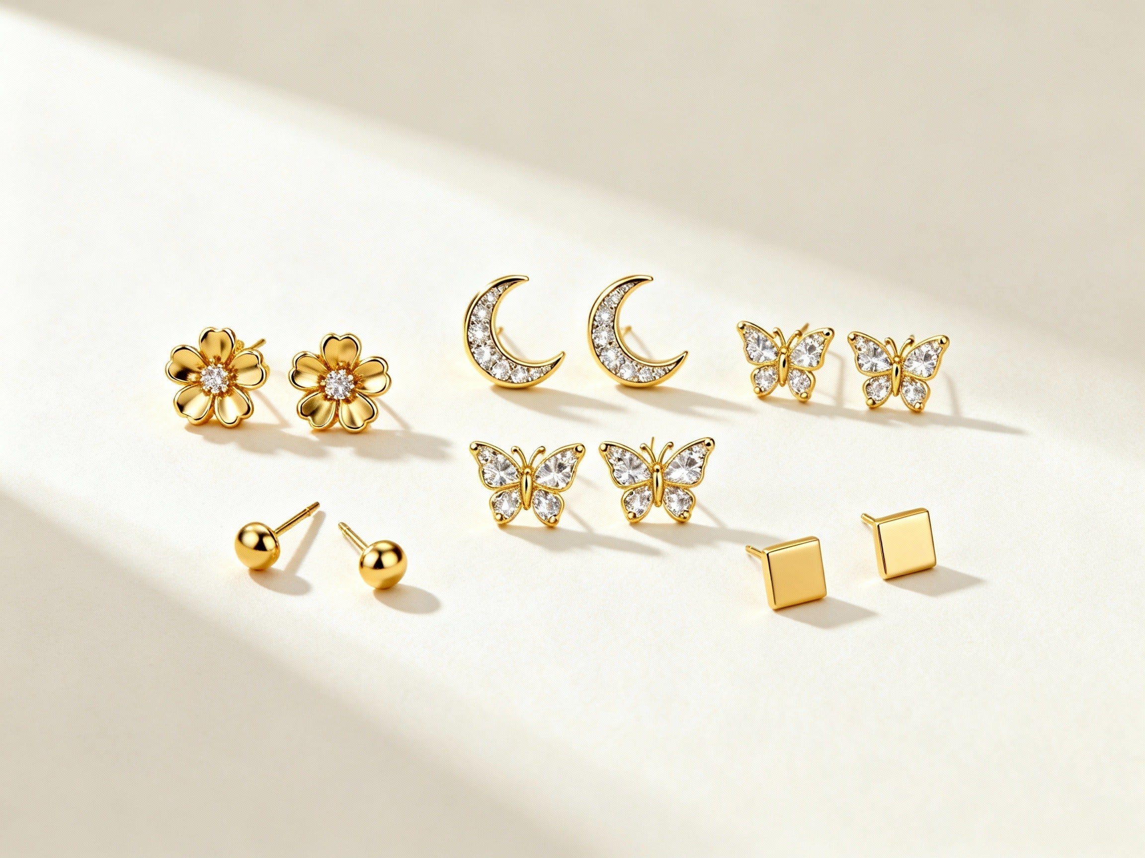 Luxury 18K PVD gold plated stud earrings featuring floral cluster, crescent moon, butterfly and geometric designs in a refined editorial layout