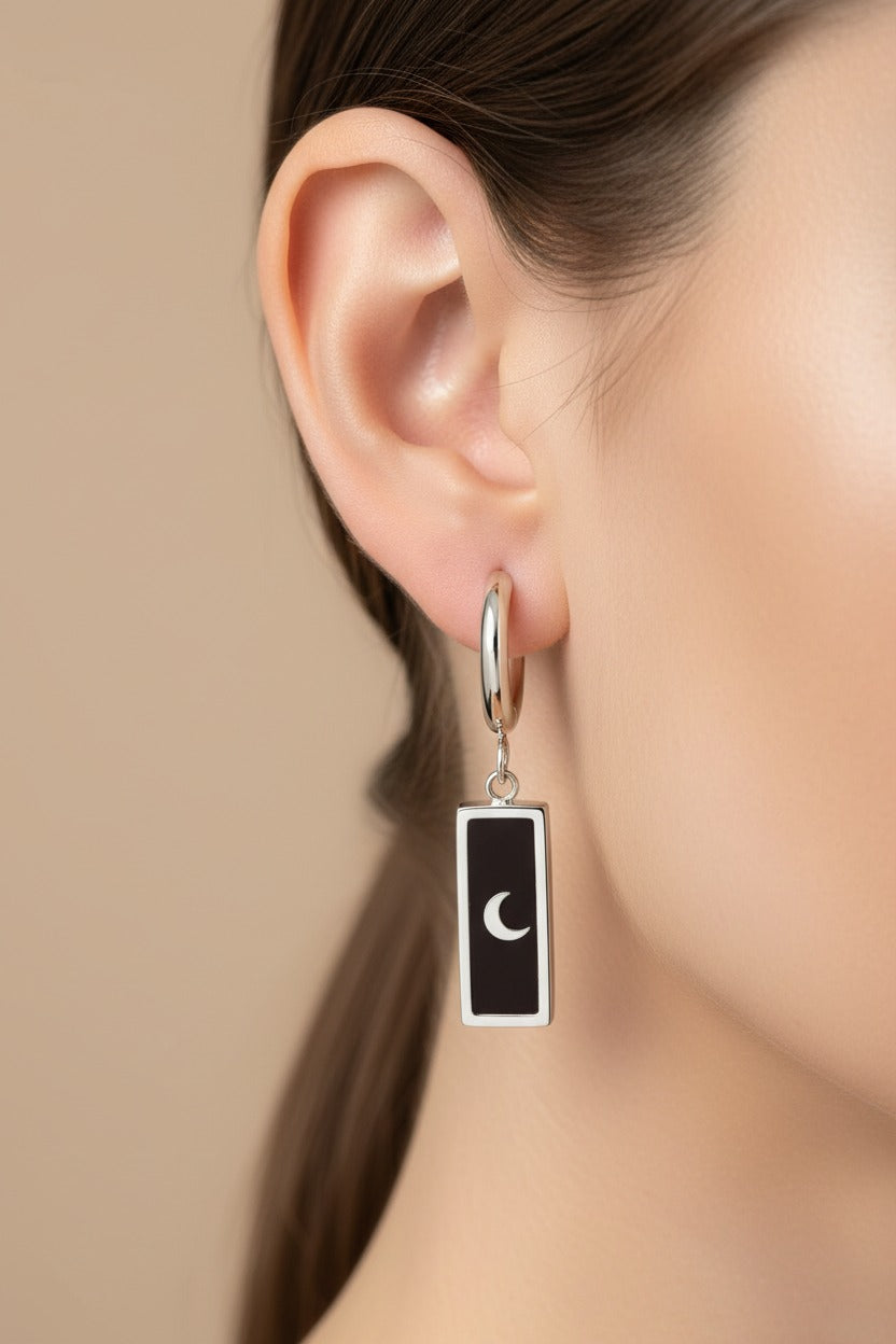 Close-up of moon and star drop earrings showcasing black enamel detailing and a polished stainless steel silver-tone finish.
