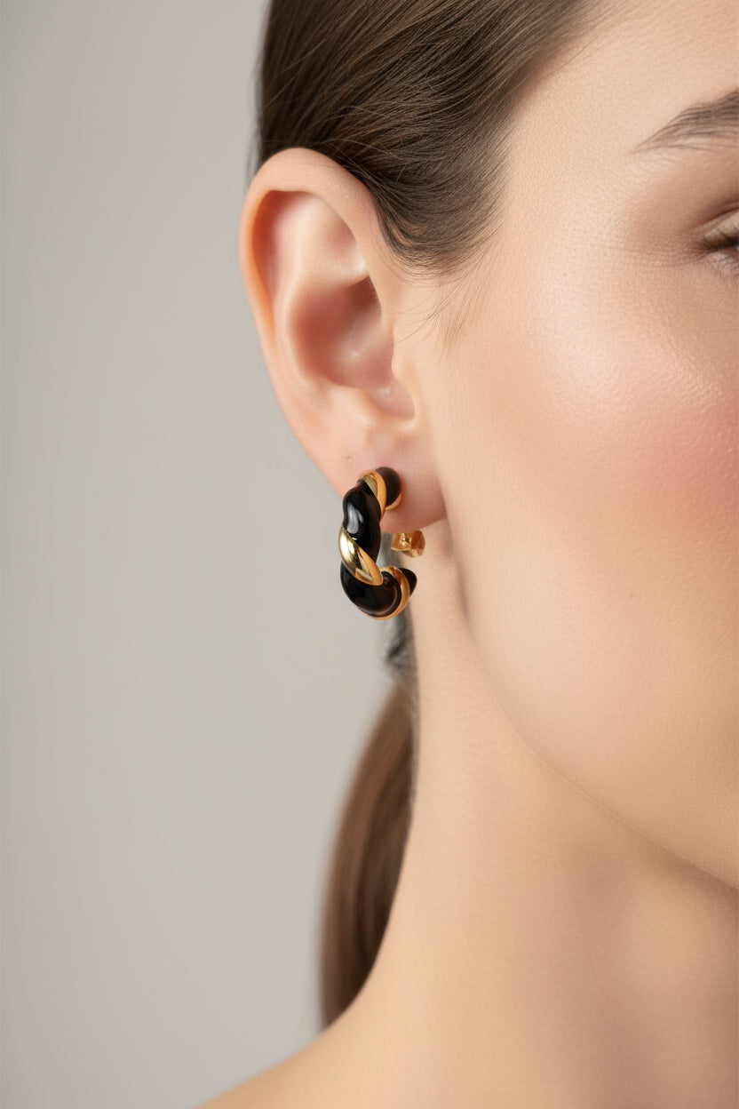 front view of twist C-hoop earrings in stainless steel with 18K PVD gold plating, showcasing black enamel detail and modern sculptural design