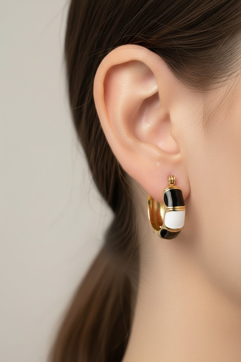 Black and white enamel hoop earrings in 18K PVD gold plated stainless steel worn on ear, modern statement design by GLISTIA