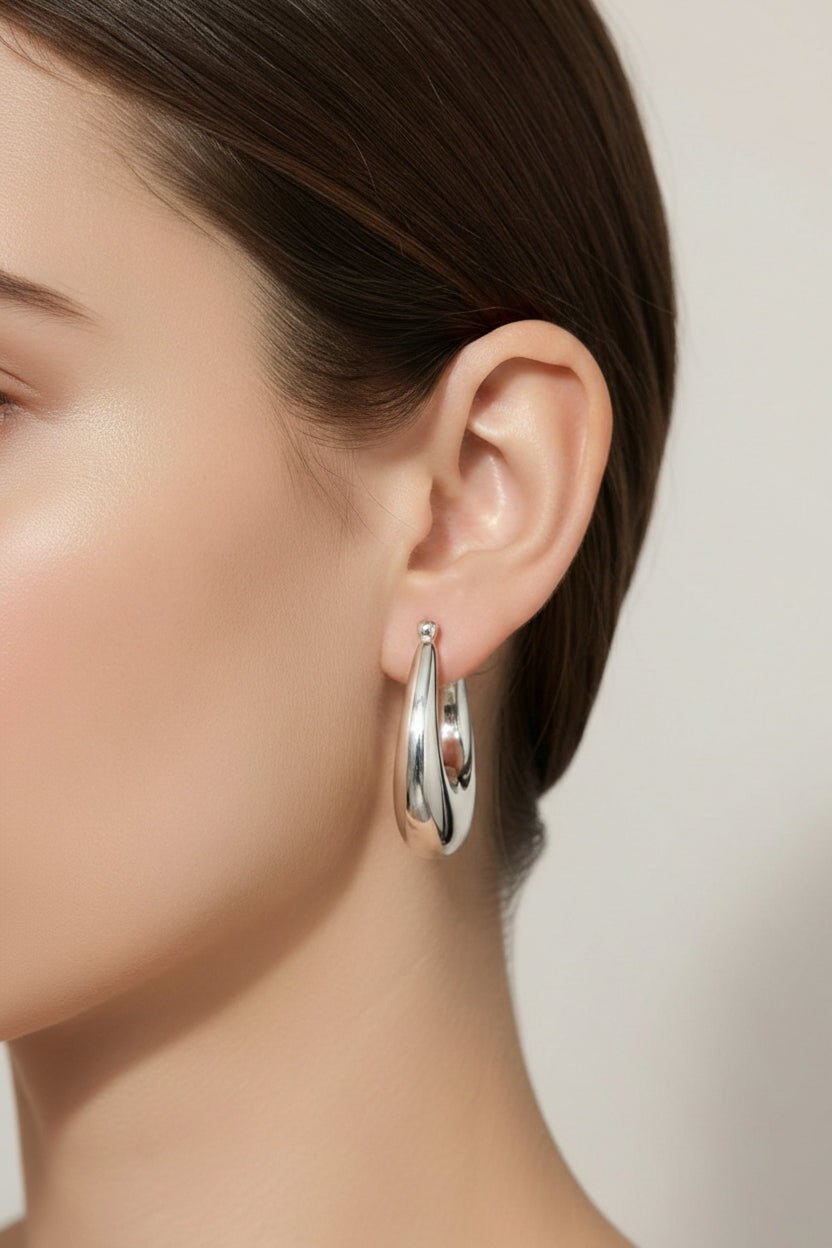 Chunky silver stainless steel hoop earrings worn on ear with polished finish and bold rounded design
