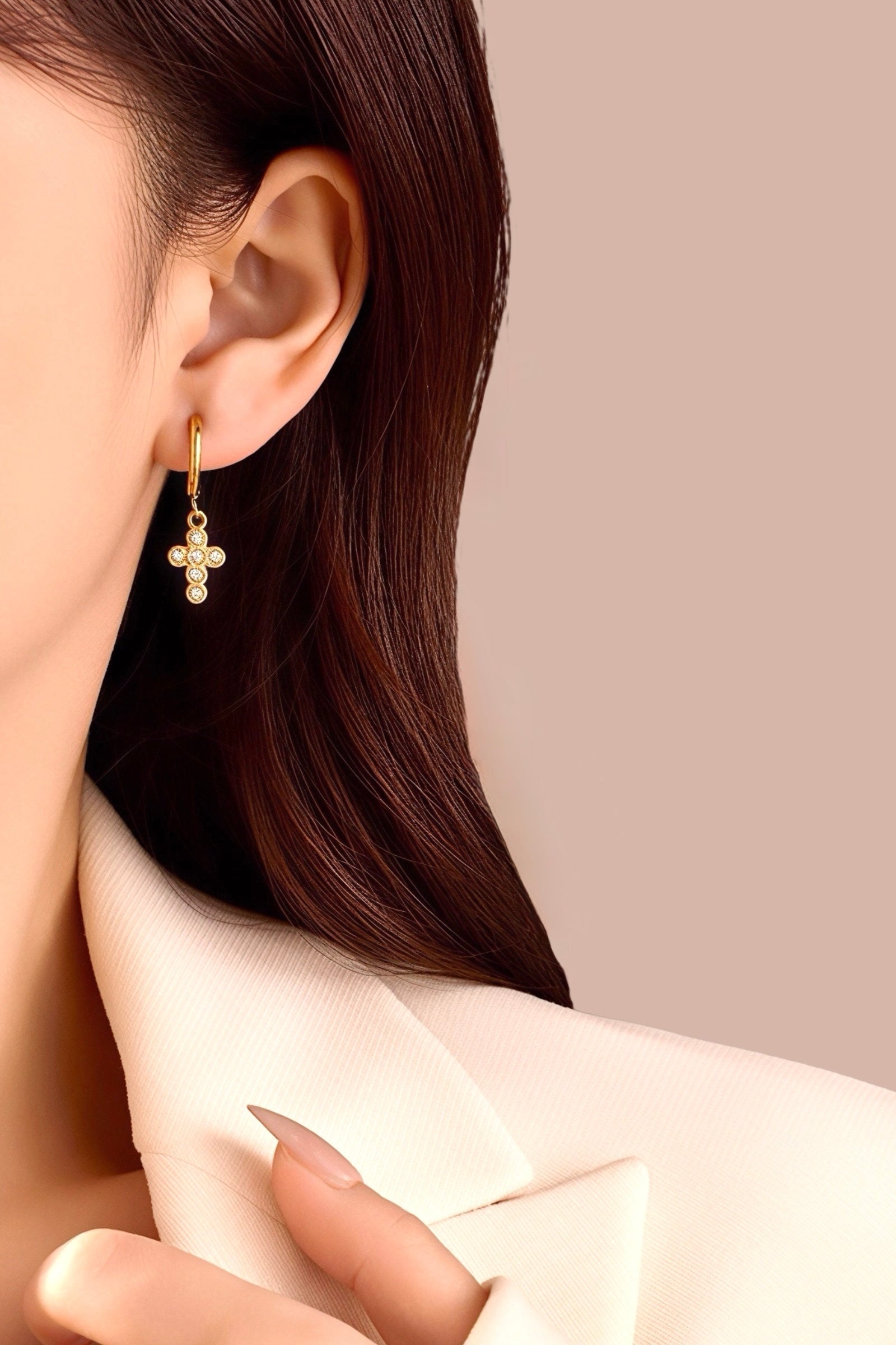 Model wearing crystal cross charm hoop earrings crafted from stainless steel with a lustrous PVD 18K gold plated finish, featuring small hoops and sparkling crystal cross pendants - GLISTIA.