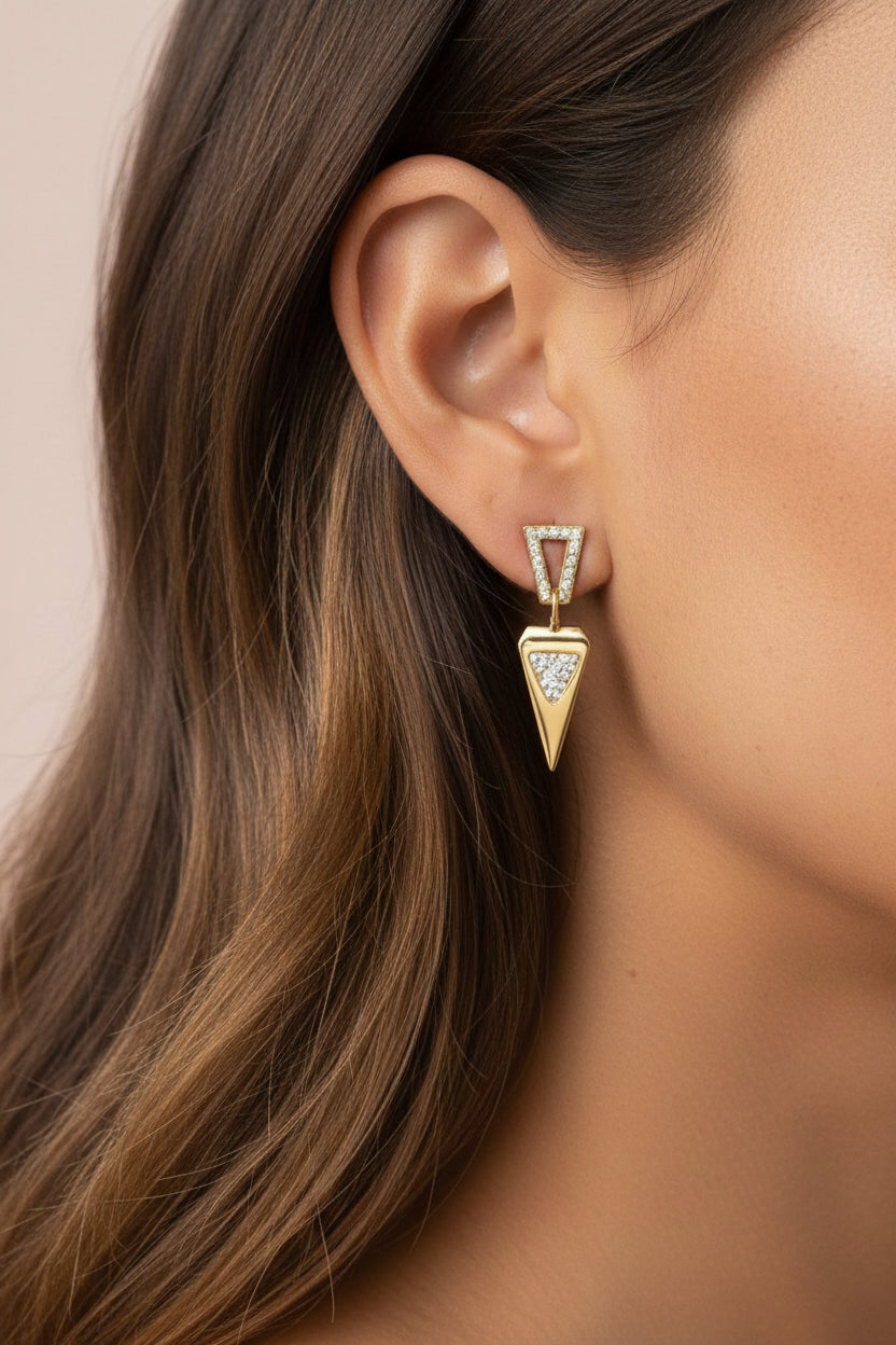 Close-up of geometric crystal triangle drop earrings showcasing polished 18K PVD gold plating and sparkling crystal detailing.