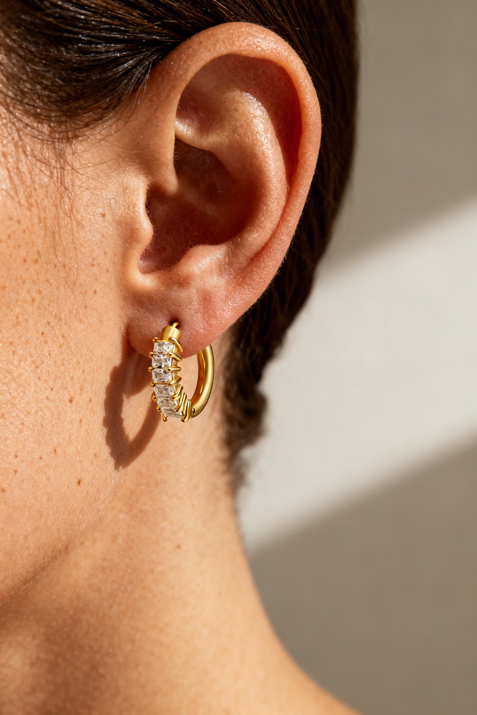 Cubic zirconia gold hoop earrings worn on ear, crafted from stainless steel with 18K PVD gold plating and sparkling CZ stones
