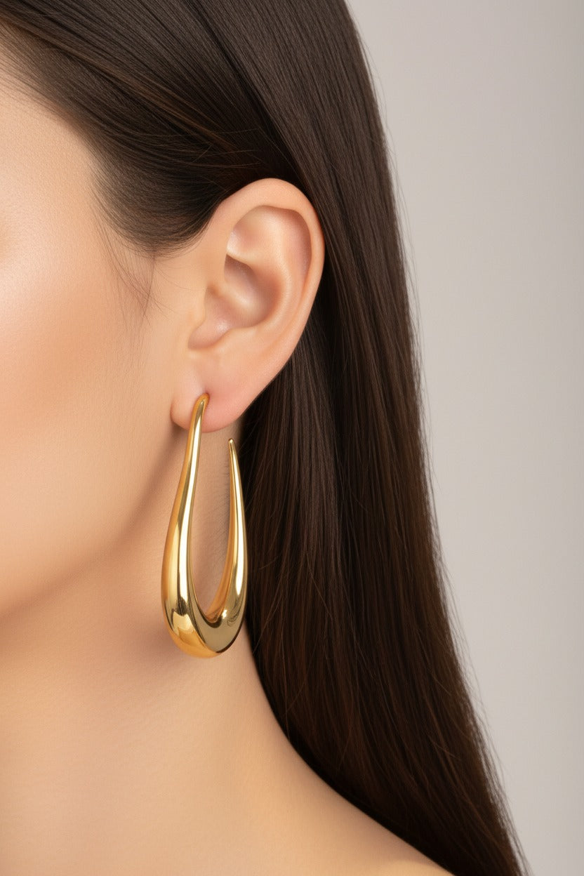 Elongated sculptural hoop earrings worn on ear, crafted from stainless steel with 18K PVD gold plating and smooth high polish finish
