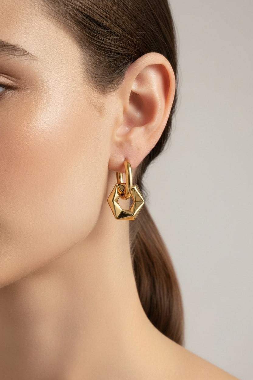 Geometric hexagon drop hoop earrings worn on ear, crafted from stainless steel with 18K PVD gold plating and a polished hexagon pendant.
