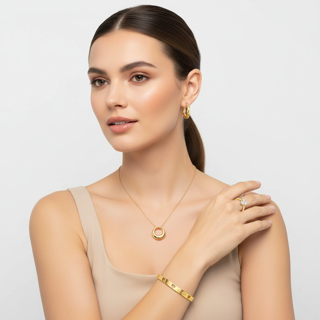 Model wearing GLISTIA 18K PVD gold-plated stainless-steel necklace, bracelet, ring and hoop earrings on a light background.