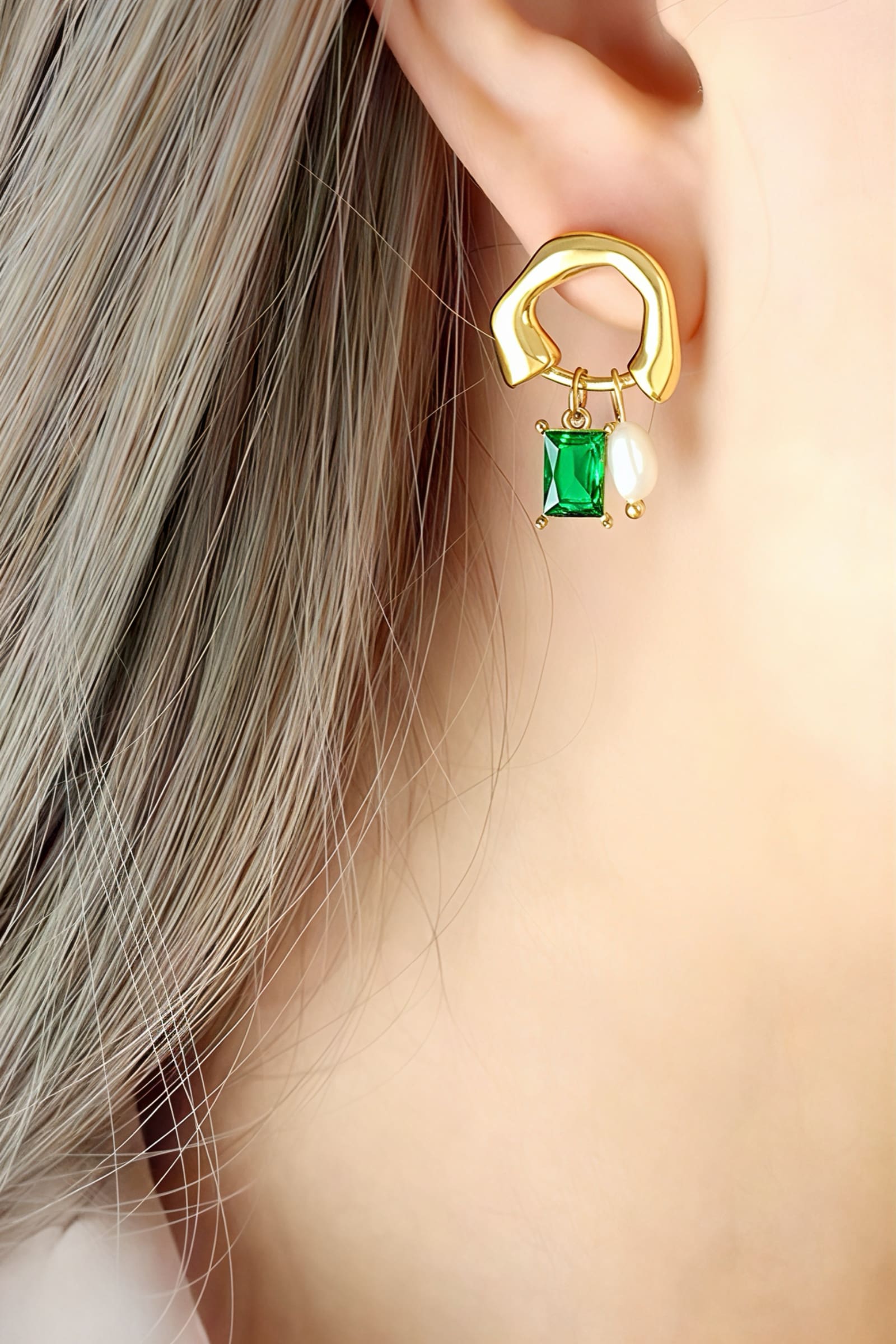 Close-up of model wearing geometric gold drop earrings featuring an emerald-green crystal and pearl charm, crafted from stainless steel with a PVD 18K gold-plated finish – GLISTIA.