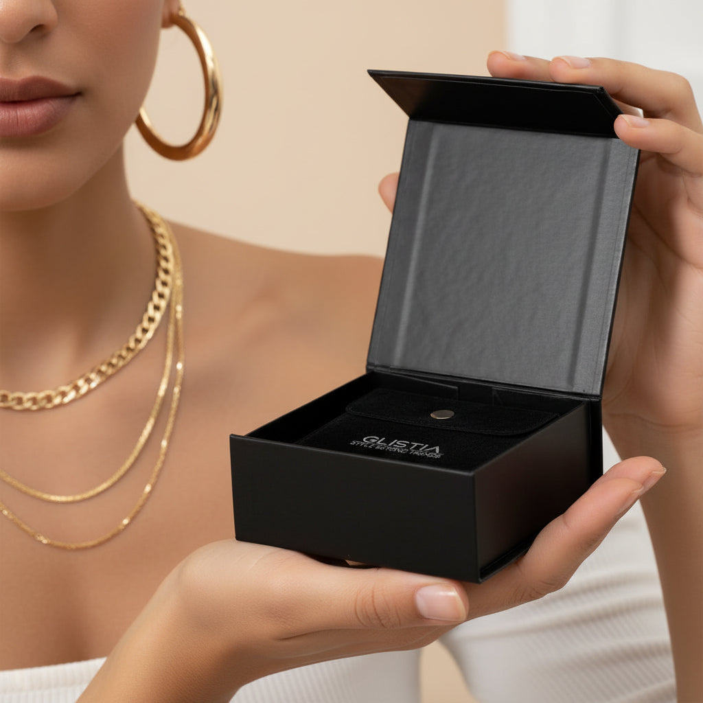 Model holding the GLISTIA luxury black magnetic jewellery gift box with velvet pouch, wearing 18K PVD gold-plated stainless-steel necklaces and hoop earrings.