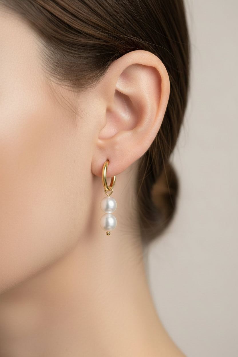Close-up of double pearl drop huggie earrings showcasing polished 18K PVD gold plating and two luminous pearl drops.