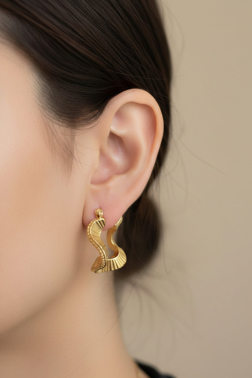 Close-up of geometric ripple hoop earrings in 18K PVD gold plated stainless steel, showcasing a modern textured design and polished gold tone.