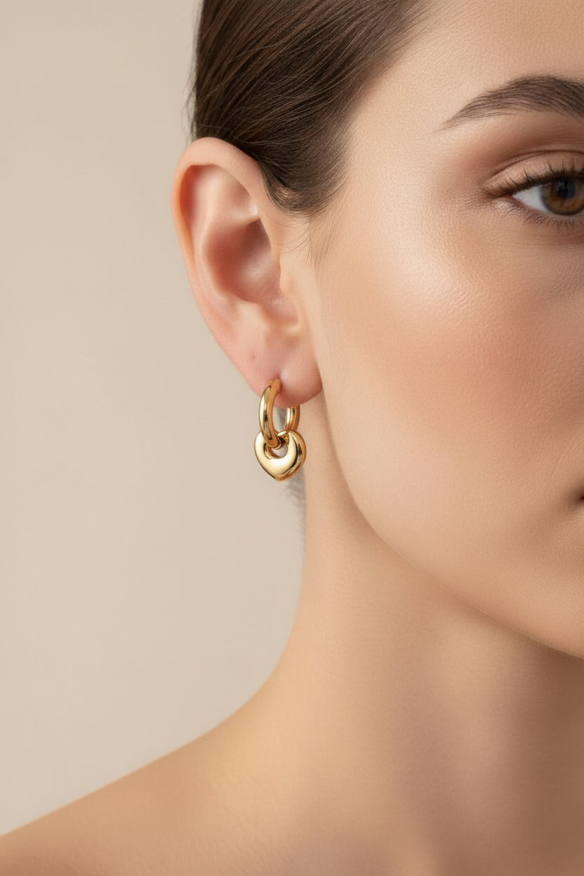 Close-up of hoop earrings with heart charm in 18K PVD gold plated stainless steel, showcasing a smooth polished finish and romantic design.