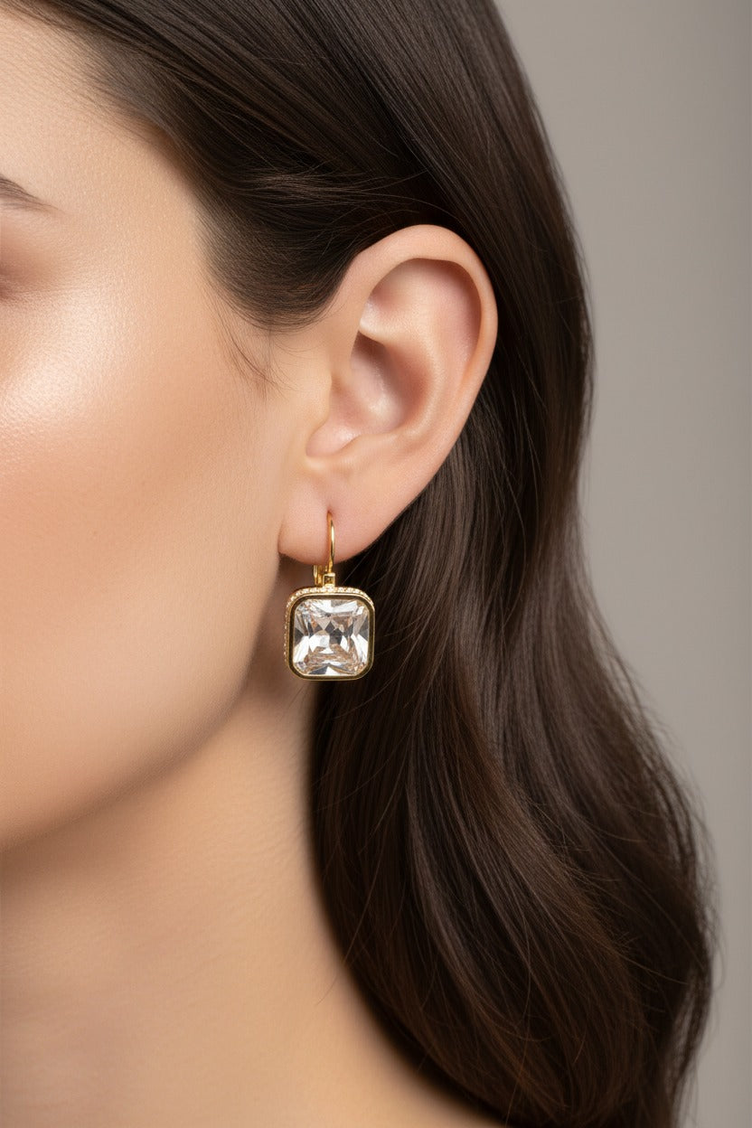 Close-up of square crystal drop earrings showcasing high-polish 18K PVD gold plating and a faceted square crystal.