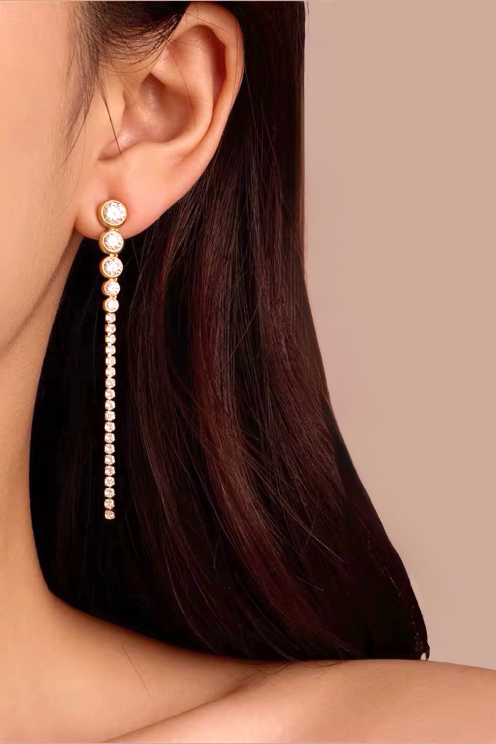 Model wearing long crystal drop earrings crafted from stainless steel with PVD 18K gold plating, showcasing a graduated line of bezel-set cubic zirconia stones for a refined and elegant look – GLISTIA.