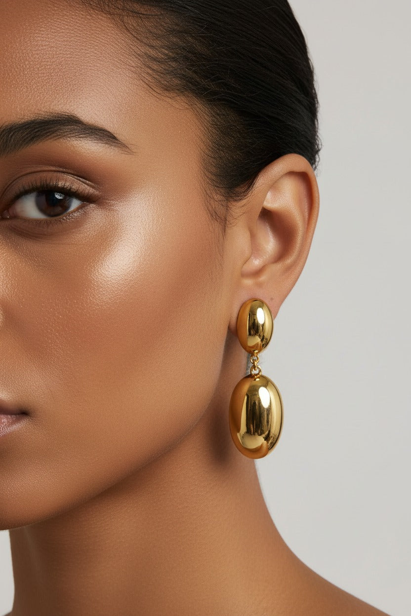 Close-up detail of long oval drop earrings in 18K PVD gold plated stainless steel with polished elongated oval drop